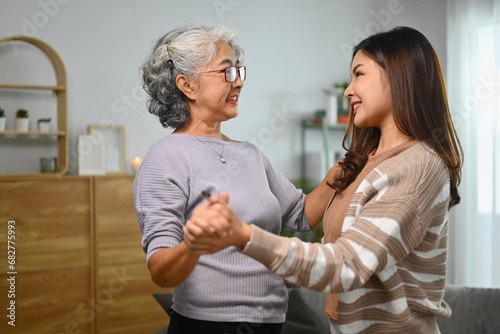 Smiling elderly mother and adult daughter dancing and spending leisure weekend time together at home