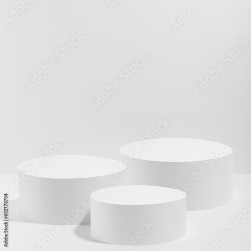 Abstract white stage with three white round podiums mockup for cosmetic products in hard light on white background. Scene for presentation cosmetic products, gifts, goods, advertising, design, sale. photo