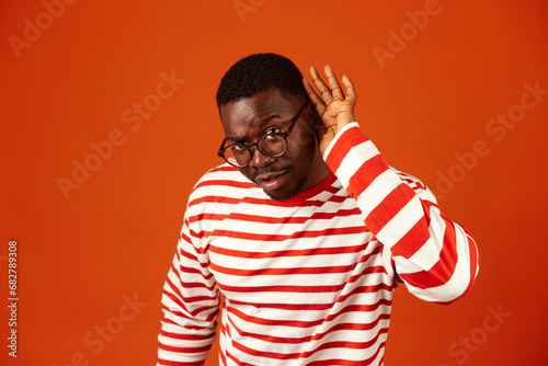 Foto Curious African-American man trying to hear you with hand gesture near ear