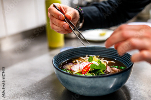 Close up of chef's hands cooking asian pho bo soup on restaurant kitchen photo
