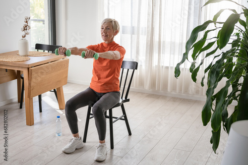 Canvas Print Smiling beautiful senior woman health instructor doing chair exercises with dumb