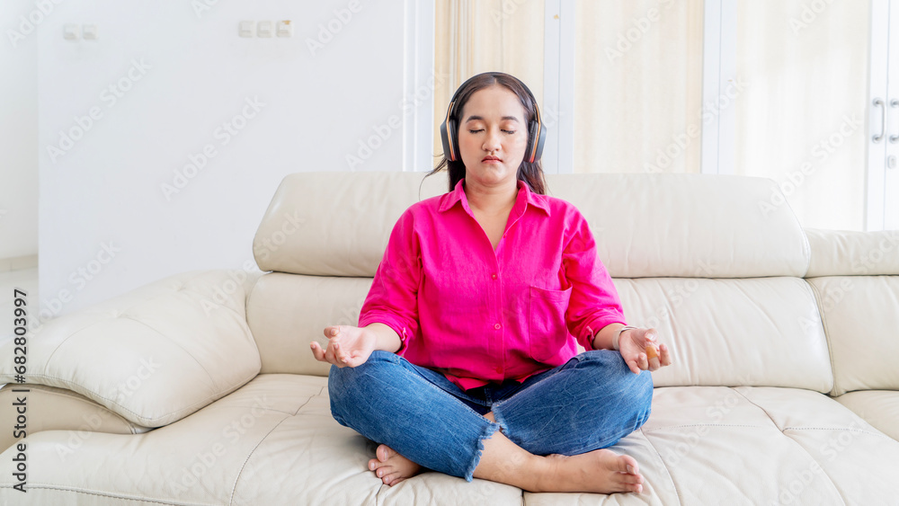 Beautiful Asian woman wearing headphone doing meditation on sofa at home Beautiful Asian woman wearing headphone doing meditation on sofa at home