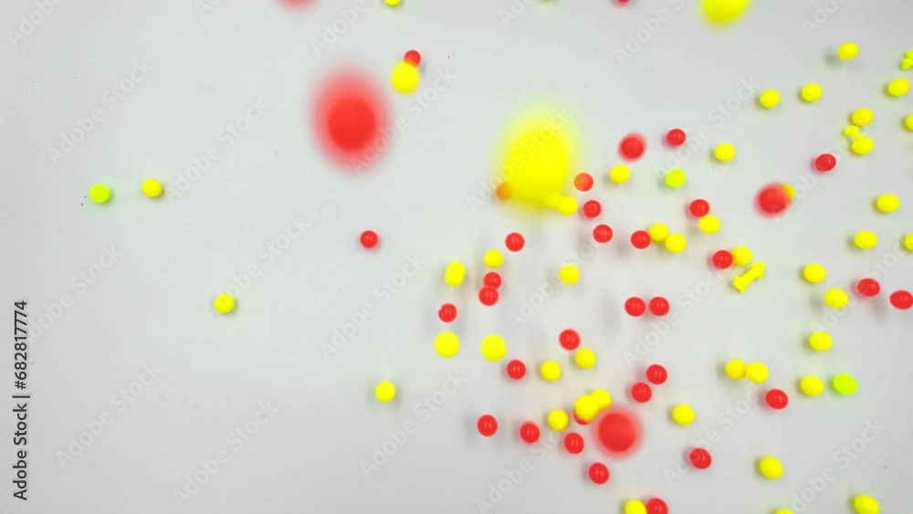 Colorful yellow and red plastic balls fall on a white surface, top view in slow motion. Colorful yellow and red plastic balls fall on a white surface, top view in slow motion.