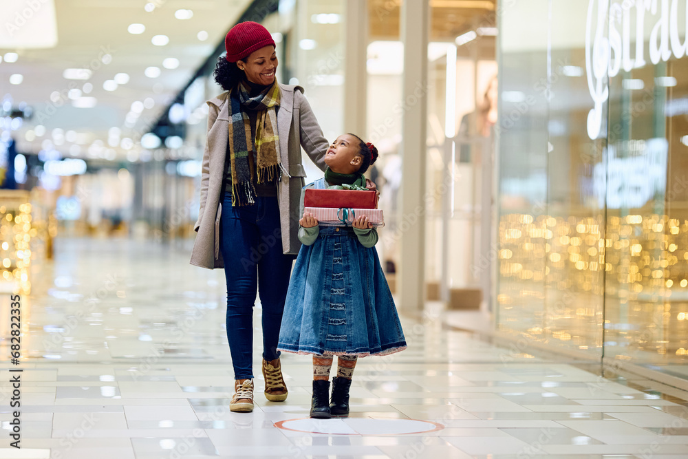 Happy black little girl Christmas shopping with her mother at the mall.