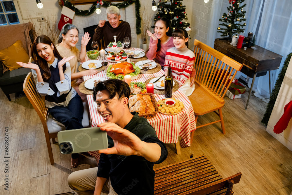Portrait of father taking selfie with smartphone of family sitting at dinner table celebrating Christmas. Photo of nice excited people taking selfie photo, laughing while having Christmas cozy dinner.