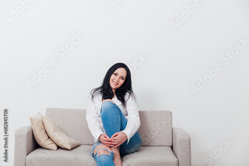 Beautiful brunette woman sitting on grey sofa in white room