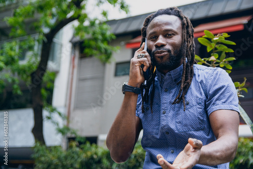 closeup of african man with dreadlocks outdoors, discussing talking on phone call photo
