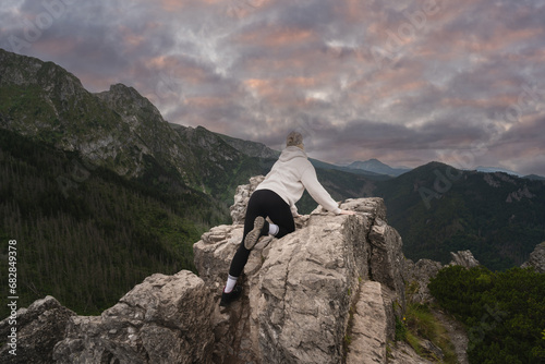 A girl climbs in the Polish Tatra mountains near the Giewont crypt at sunset, view from the back.