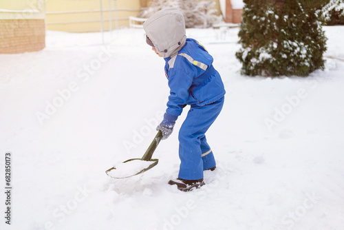 4 years old boy kid with a shovel snowing away the path in the yard. Child is playing outdoor on the winter season