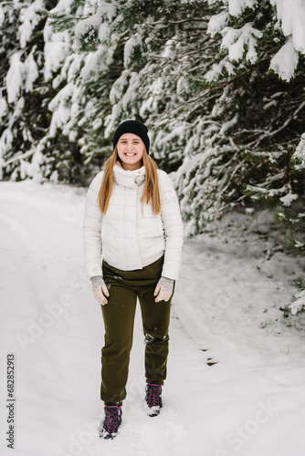 Winter smiling woman among snowdrifts. Happy girl playing in winter park, spending holidays. Woman walk in mountain country in snowy forest together. Female having fun walking in snow nature.