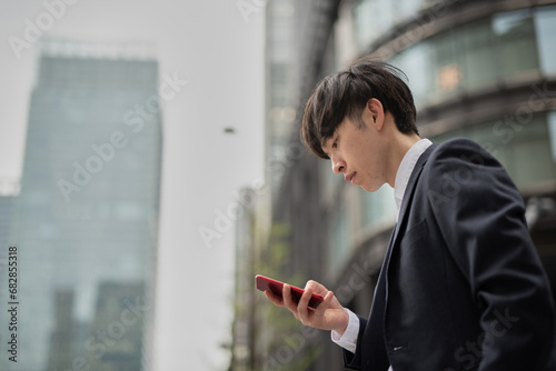 オフィス街の通りでスマートフォンを見る若いビジネスマン