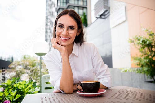 Portrait of cheerful gorgeous girl hand touch chin toothy smile enjoy aroma coffee street cafe outside