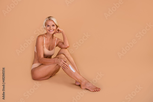 Full body portrait of perfect shape attractive lady apply lotion legs empty space isolated on beige color background