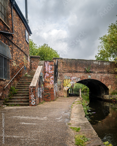 A graffitied old brick bridge over a canal with a staircase leading up to the road
