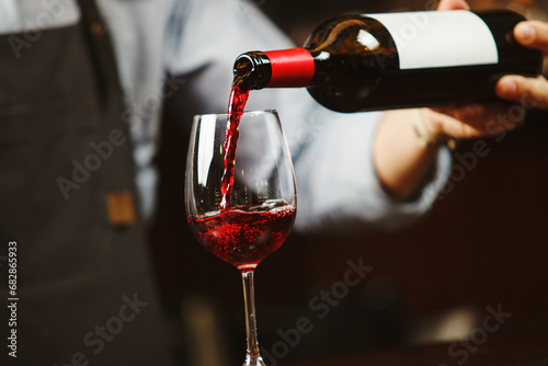Waiter pouring red wine into wineglass. Sommelier pours alcoholic drink