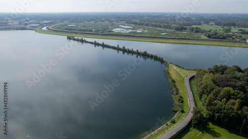 This aerial image captures the serene boundary where land meets water. A narrow strip of land carves its way through the calm lake, creating a natural divide that appears almost like a soft