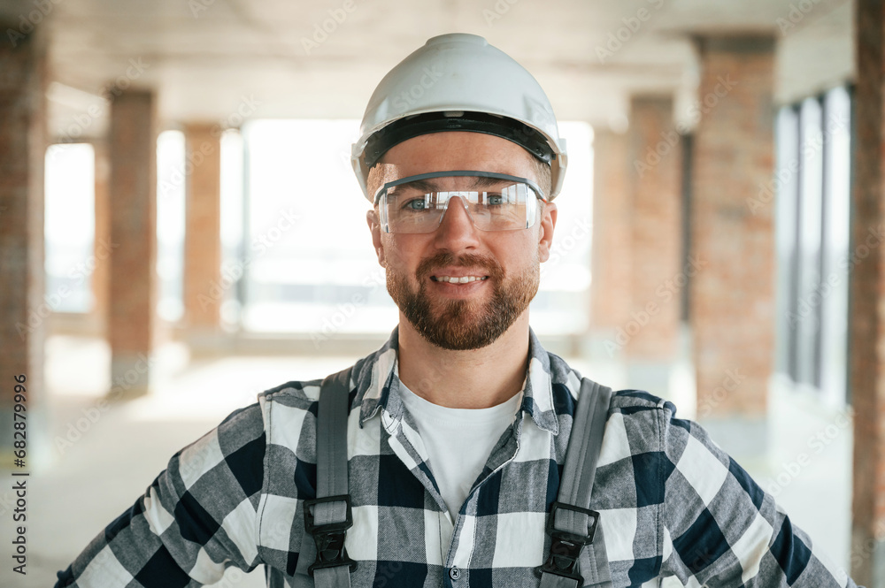 Positive smiling construction worker in uniform in empty unfinished room Positive smiling construction worker in uniform in empty unfinished room