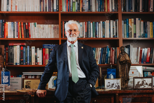 Experienced mature rector confidently posing in university library surrounded by books. Successful academic leader, university owner, and professor in the 60s or 70s. photo