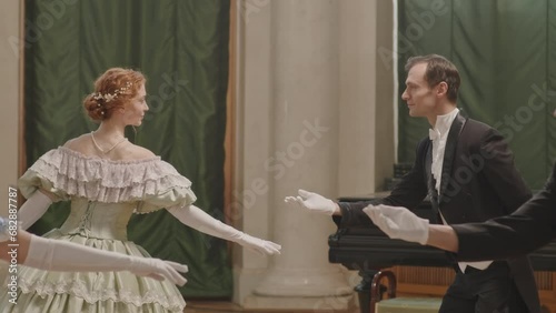 Medium slowmo shot of two Caucasian aristocratic men stretching their hands while inviting women to dance with them during ceremonial reception with ball photo