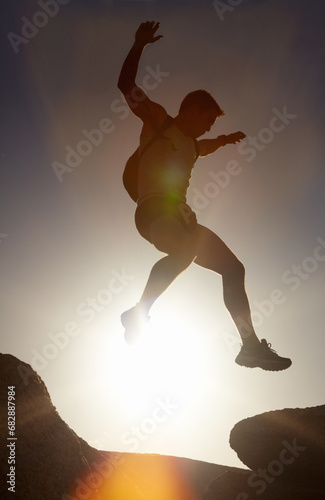 Man, silhouette and jump on rock at sunset with freedom, adventure and challenge on mountain or cliff. Climbing, hill and person with fearless leap in hiking, exercise or energy at with sky in summer photo