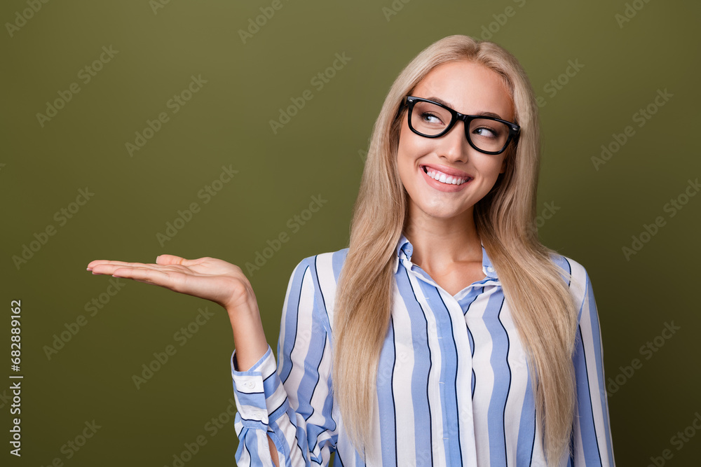 Photo portrait of blonde lovely young lady palm hold look empty space wear trendy striped garment isolated on khaki color background Photo portrait of blonde lovely young lady palm hold look empty space wear trendy striped garment isolated on khaki color background
