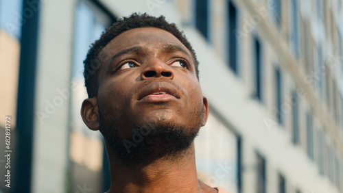 Close up pensive thinking ethnic man looking around outdoor business student guy look up on urban building think thoughtful African American male tourist contemplate outdoors outside lost in city photo