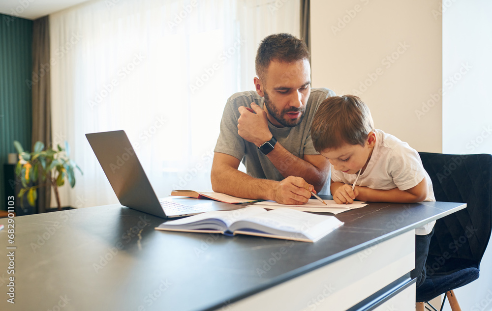 Writing the homework. Father and son are at home by the table Writing the homework. Father and son are at home by the table