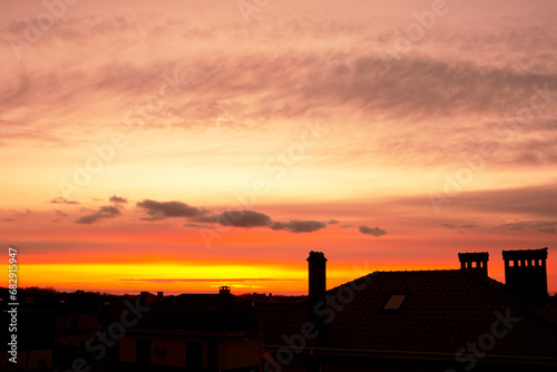 Roofs of houses against the backdrop of a beautiful sunset. Orange sky with beautiful cumulus clouds. Textured sky background at sunset.