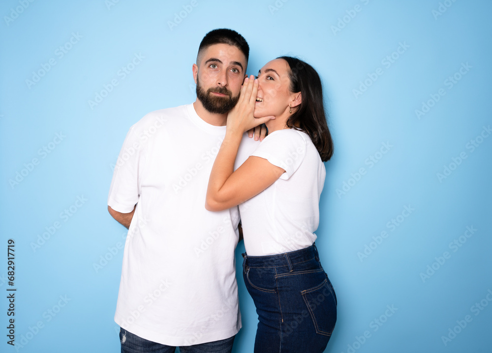 Brunette whispering secret to her boyfriend on blue background Brunette whispering secret to her boyfriend on blue background