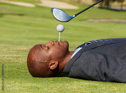 Black man, face and lying on golf course with tee in mouth for hole in one on green grass or field. African male person, golfer or assistant holding ball with club hovering for swing or hit on pitch