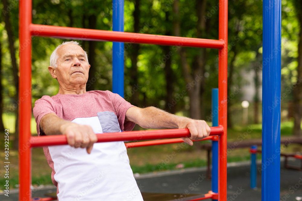 Elderly man doing fitness on sports ground equipment in park