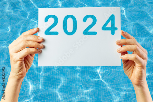 2024, Woman holding cardboard with number 2024 on background of faded lights. Happy New Year