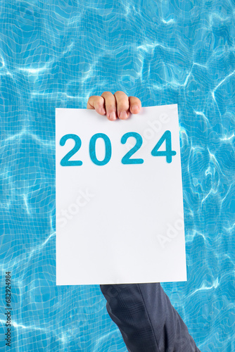 2024, Man holding cardboard with number 2024 on background of faded lights. Happy New Year