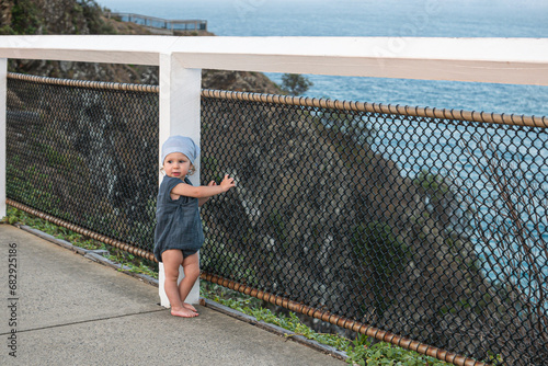 Little girl standing in front of a fence in front of ocean 