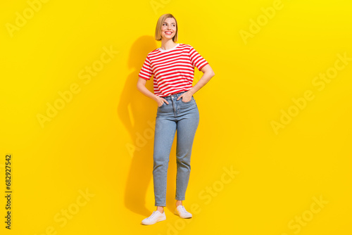 Full size photo of satisfied girl wear stylish t-shirt arms in pockets look at offer empty space isolated on bright yellow background © deagreez