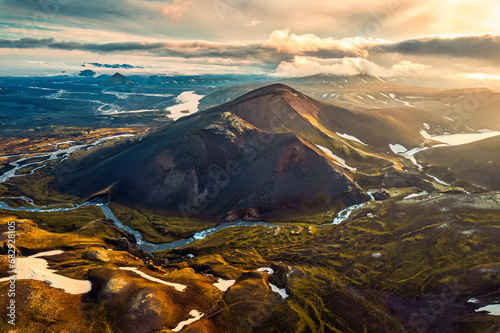 Sunset shines over volcanic mountain with river flowing in Icelandic Highlands during summer at Iceland