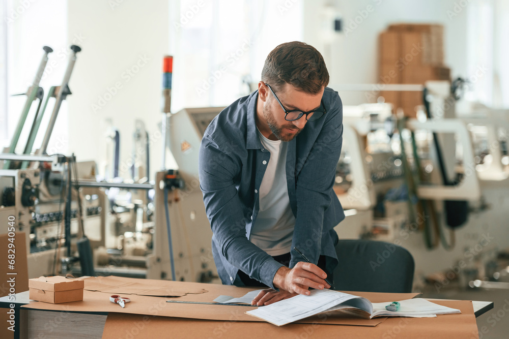 Table, document on it. Handsome man is working at the factory of creating eco boxes Table, document on it. Handsome man is working at the factory of creating eco boxes