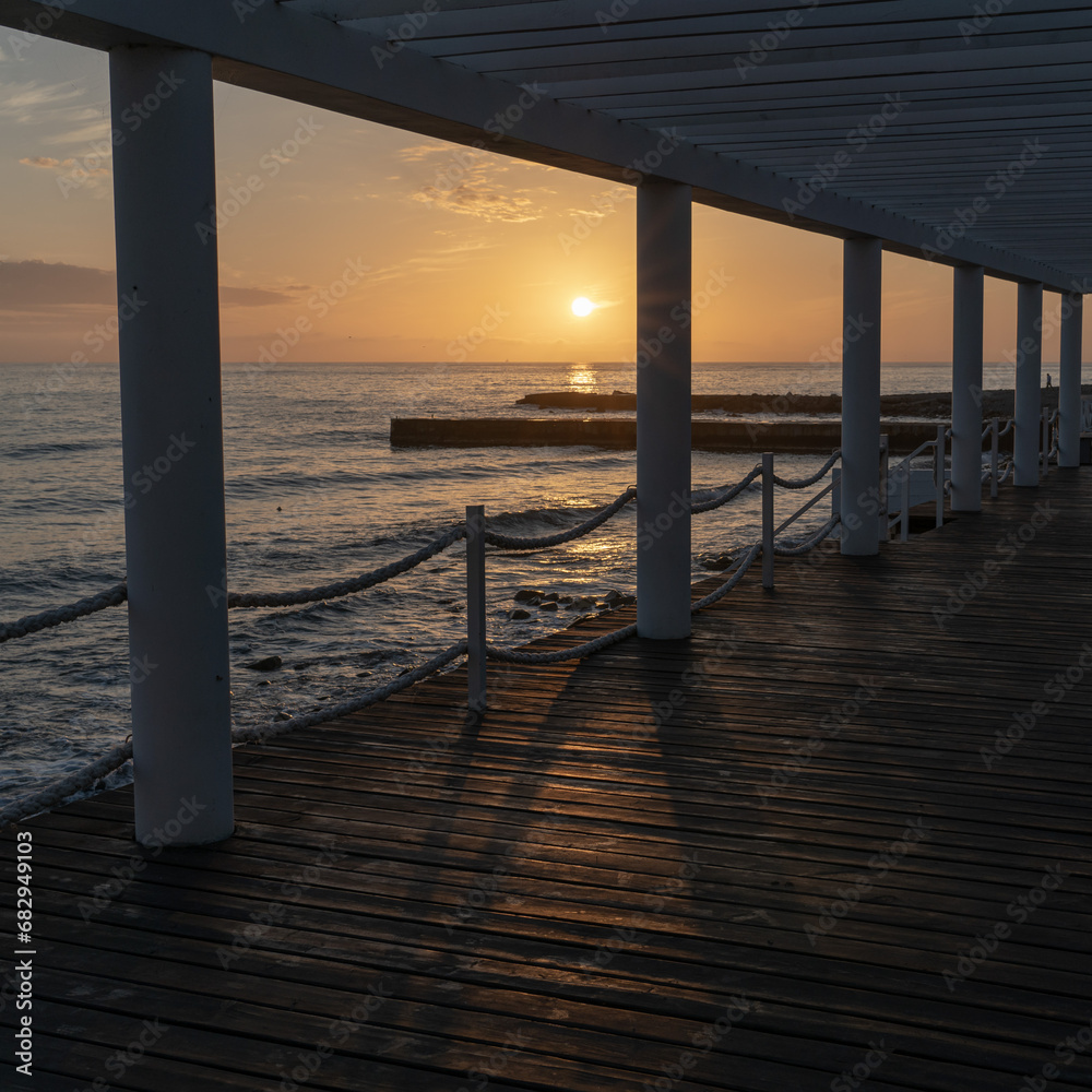 Pier and breakwaters in the rays of the setting sun at sunset. Autumn seascape. Pier and breakwaters in the rays of the setting sun at sunset. Autumn seascape.