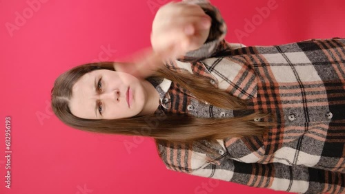 Vertical footage of serious confident young caucasian woman wearing shirt showing stop, one finger gesture, taboo sign, standing over red color background wall in studio. No, people emotion concept photo