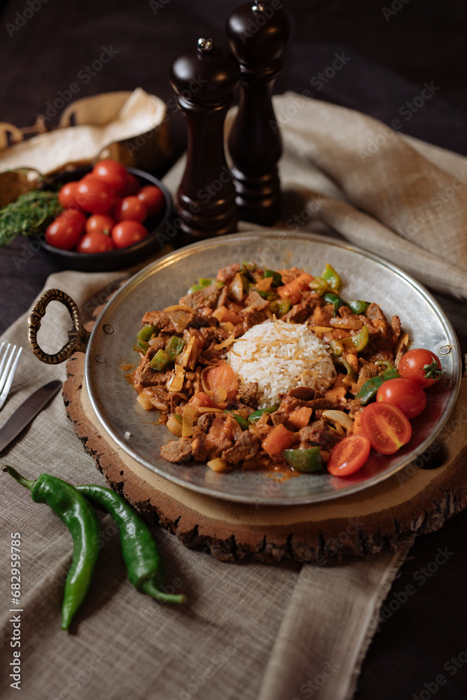Pilaf. On a plate there is rice with meat and vegetables. National cuisine. The dish is garnished with fresh green peppers, tomatoes and fresh herbs. Plov
