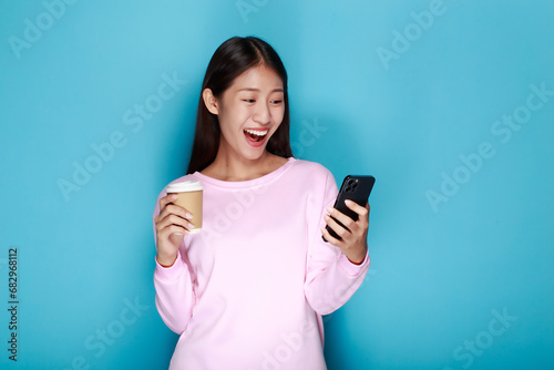 Beautiful young woman in a light blue background, happy and smile, posting in stand position, A beautiful woman poses very cheerfully and happily while holding a cell phone in her other hand.