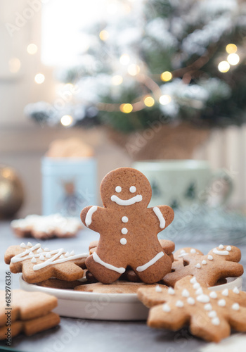 Close up of Christmas sugar cookie in a gingerbread man shape decorated with royal icing glaze. Cozy festive ambiance of greetings holidays with xmas tree decoration lighting bokeh in background