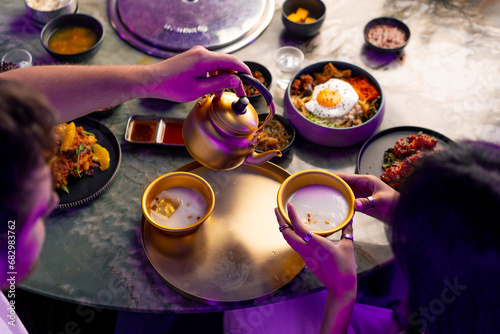 close-up of a girl pouring a traditional Korean low-alcohol drink makoli from a golden teapot into a cup with ice in a restaurant