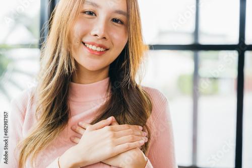 Beauty Asian young woman touching her chest for thanking at home, happy charming female smiling hold hands chest near heart honest with grateful gesture