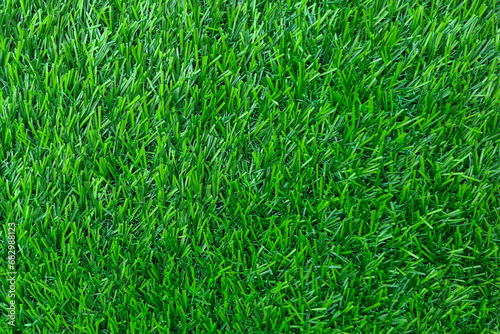 Close-up of a patch of artificial grass. The grass is green and has a smooth, plastic surface. The blades of grass are all the same length and thickness, and they are evenly spaced apart