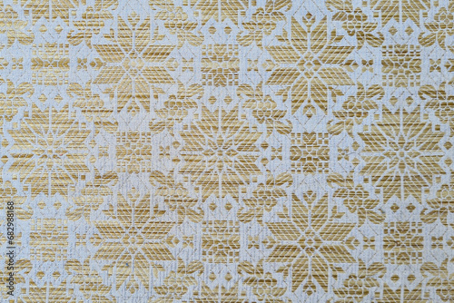Close-up of a white fabric with a gold pattern. The fabric is smooth and silky, with a slight sheen. The gold pattern is made up of delicate swirls and flourishes