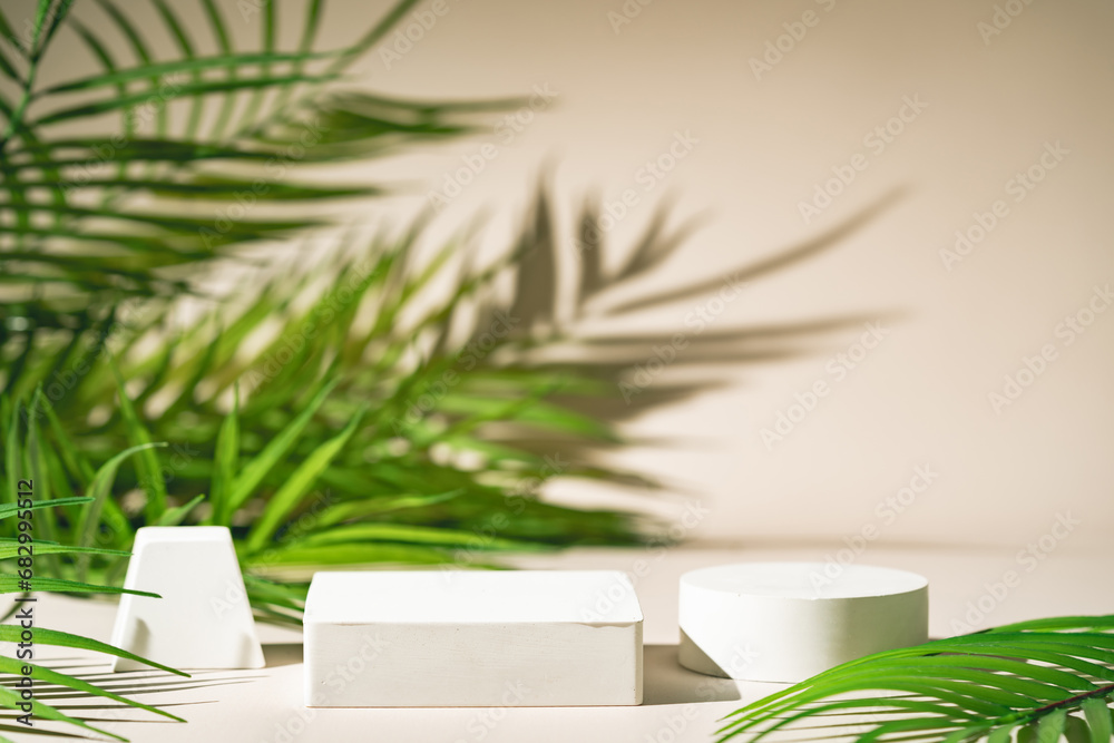 Cosmetic background for product presentation. White empty plaster podium with green palm leaves and shadows on biege background