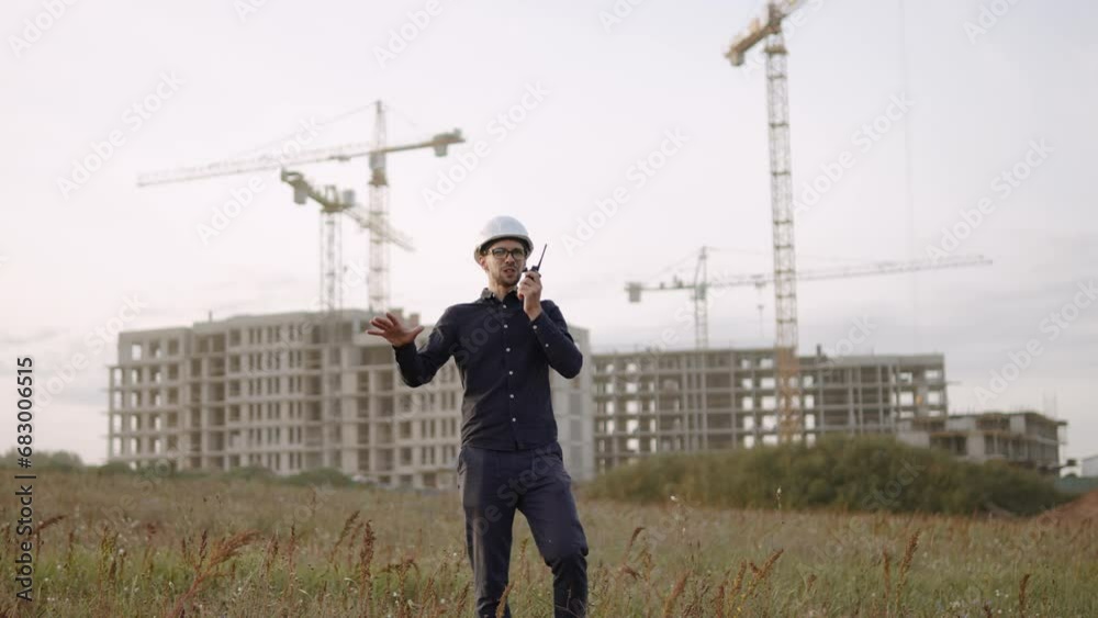 Portrait of slender foreman in hard hat at construction site sharing plans and motivating workers through walkie-talkie. Positive improvement of team spirit in team work during the working day.