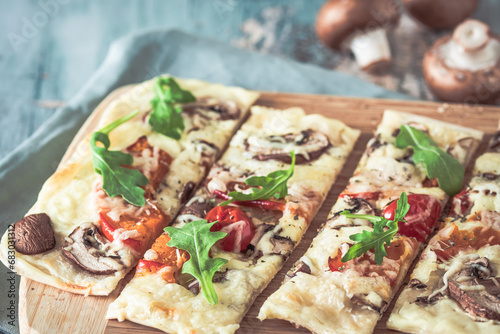 Freshly baked flammkuchen, traditional french tarte flambee or german pizza in a vegetarian recipe with mushrooms, cream cheese, tomatoes and arugula, on  light greenwooden board and table photo