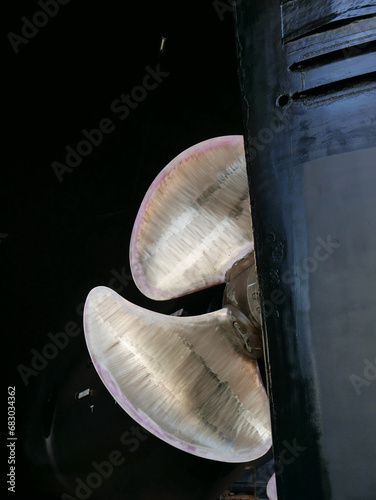 black gold. ship in dry-dock out of water. bronze polished propeller on black painted hull, details of rudder.